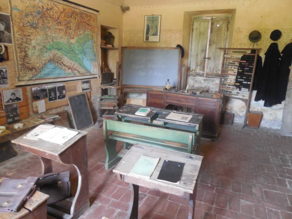 Schulunterricht in Italien in der Nachkriegszeit; zu sehen sind Schulbänke, ein Tafel, eine Italienkarte und ein Recheninstrument
